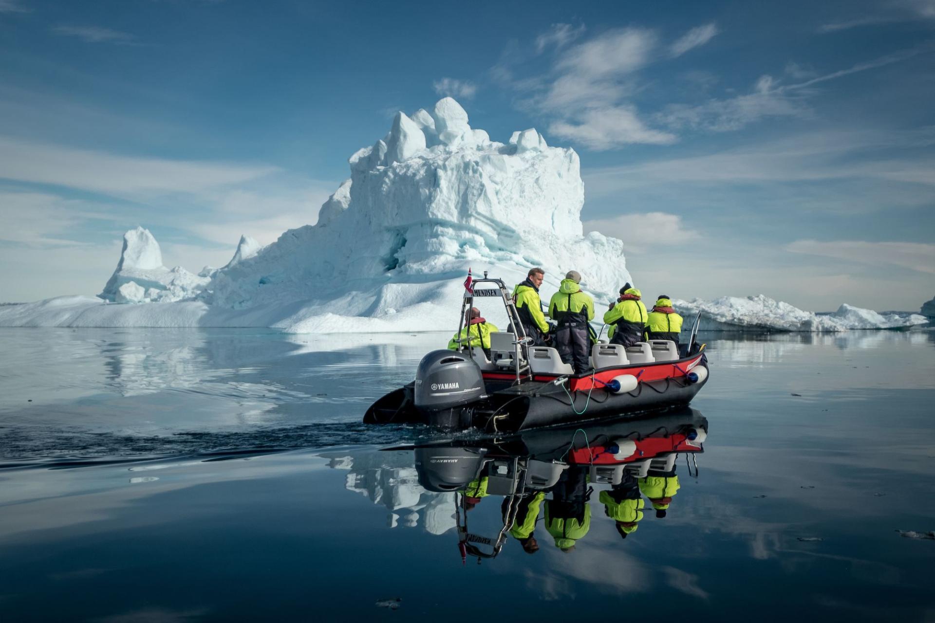 An expedition boat passing an iceberg on still water in Disko Bay, Greenland
